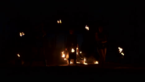 Slow-motion:-Professional-fire-performance-three-women-in-dripping-clothes-dance-and-spin-with-flaming-torches-and-a-man-with-flamethrowers-in-the-background.